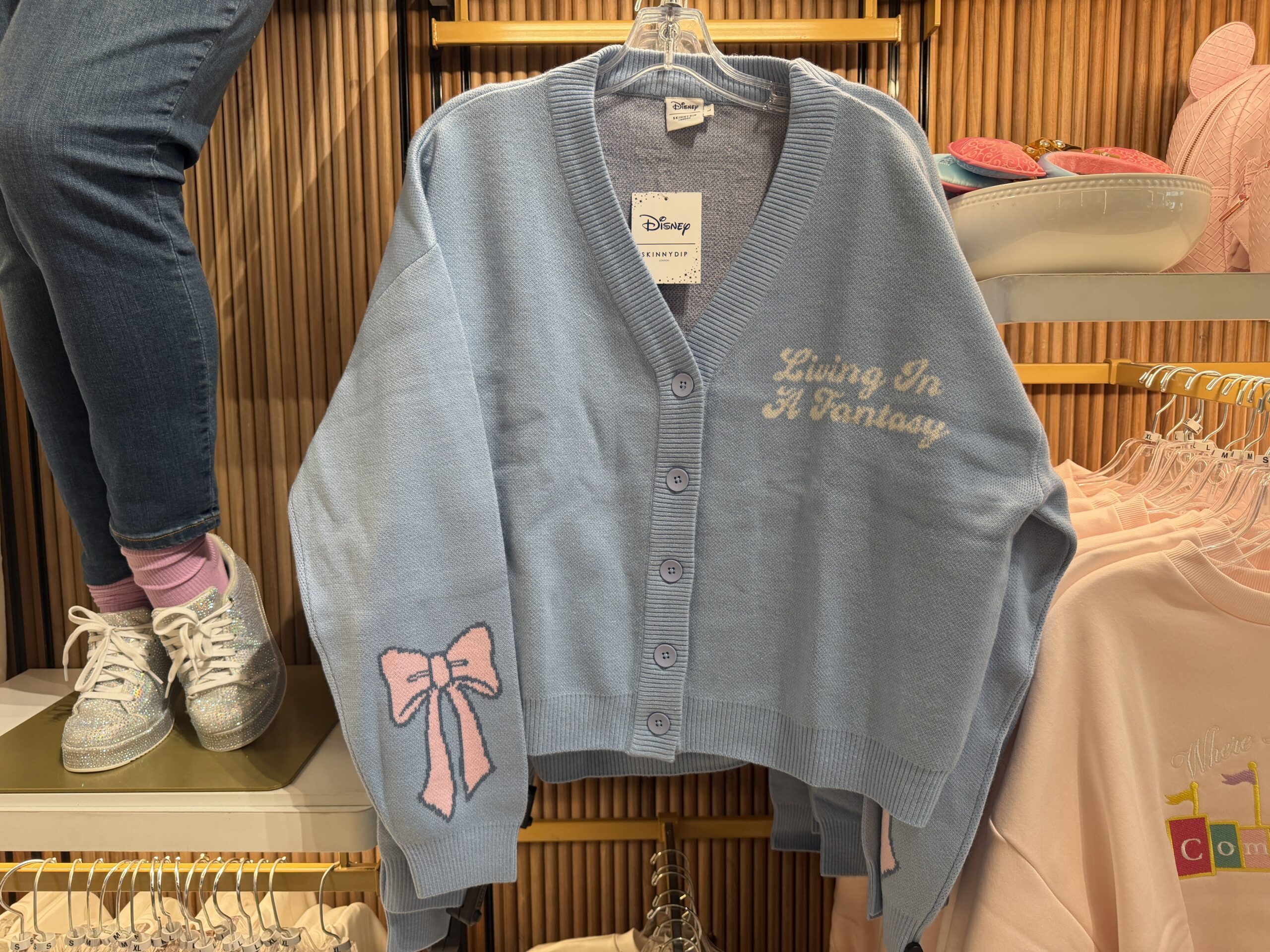 This cropped cardigan is light blue with matching blue buttons. "Living In A Fantasy" is shown in white cursive on one side of the chest.