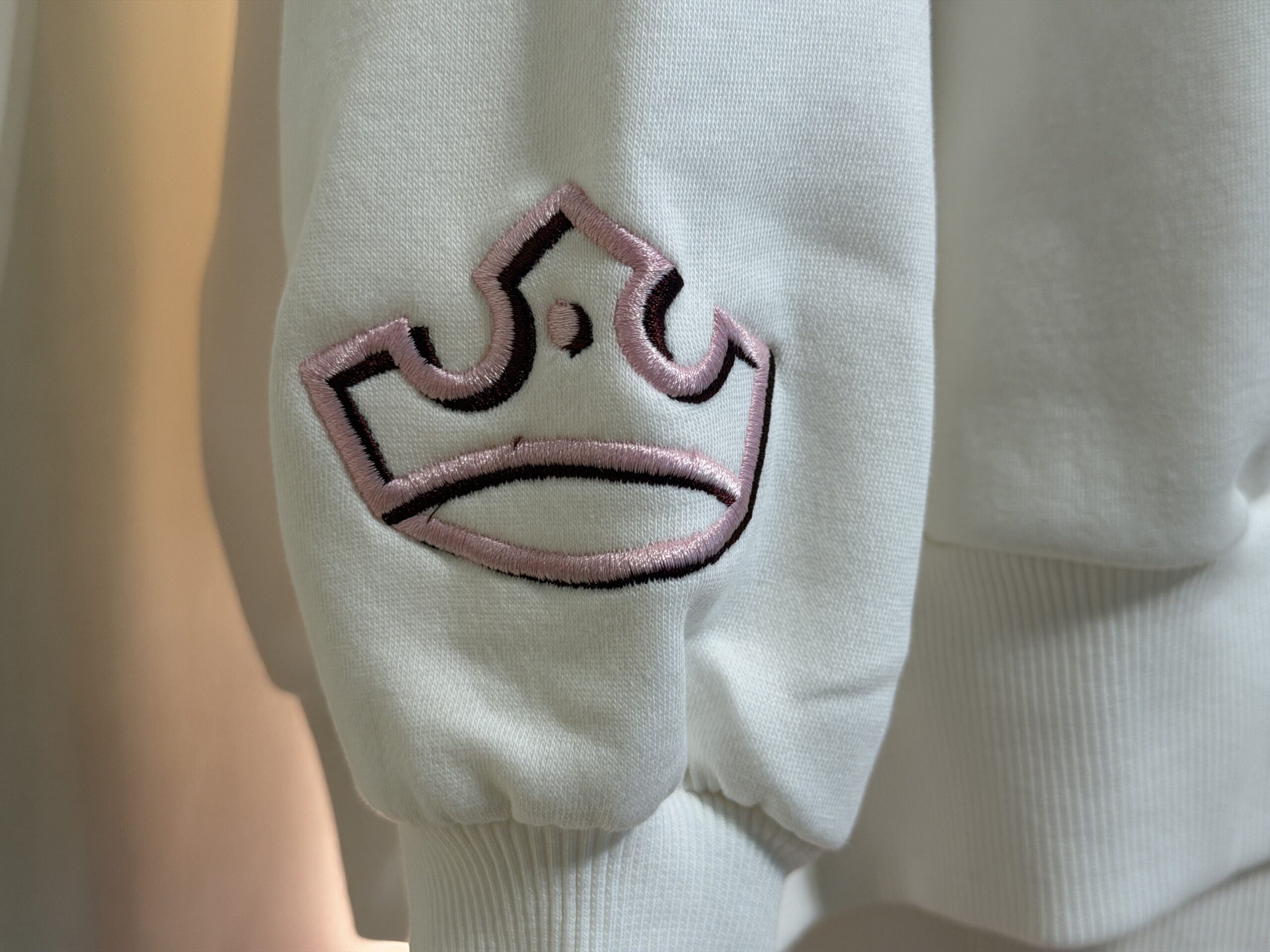 This white sweatshirt has "Once Upon a Time" embroidered on a pink scroll, surrounded by clouds and a pink bow. A pink crown edged in black is embroidered on one sleeve end.