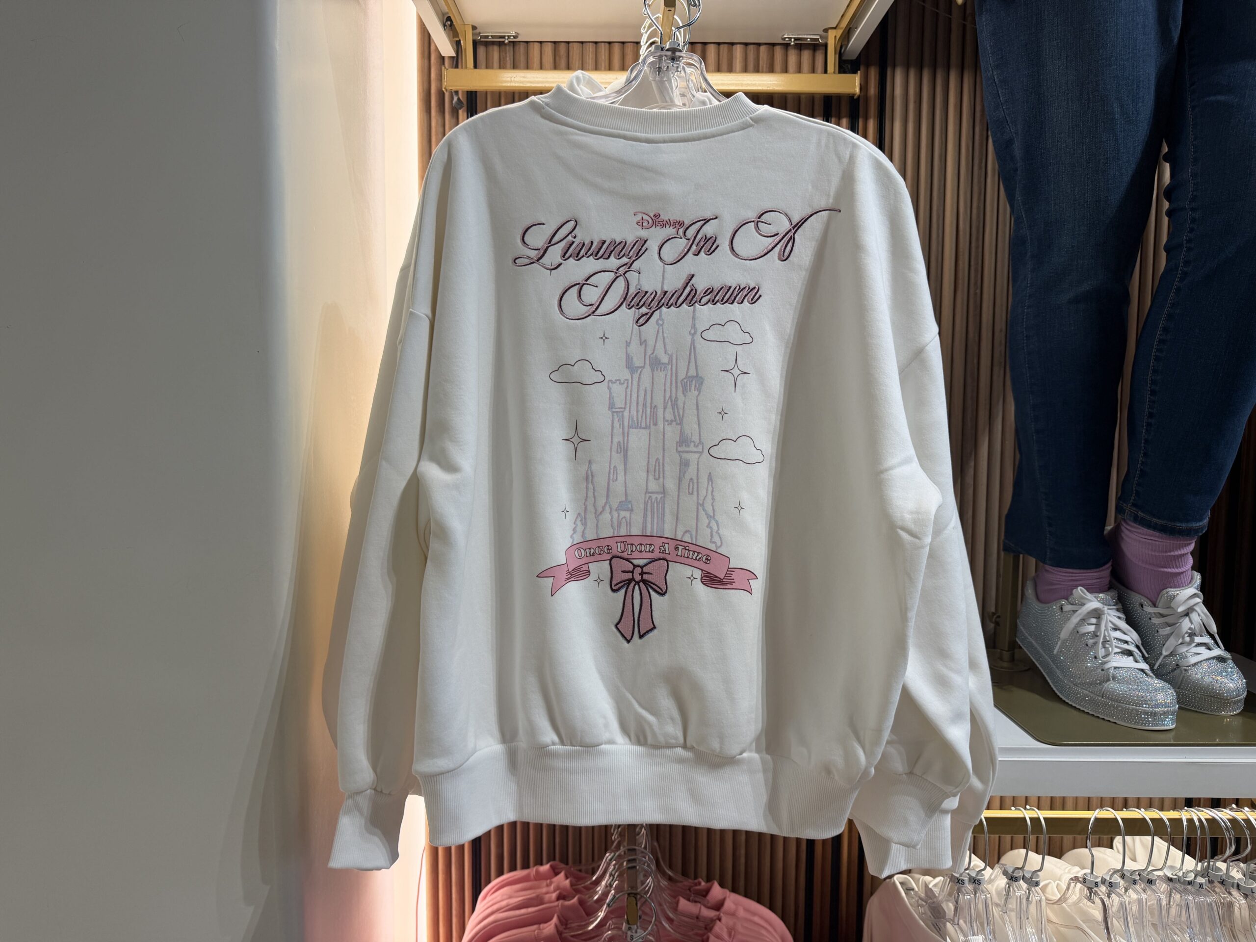 The back of the sweatshirt has a large castle surrounded by clouds and stars. "Living In A Daydream" is embroidered above the castle, while the same "Once Upon a Time" scroll design is below.