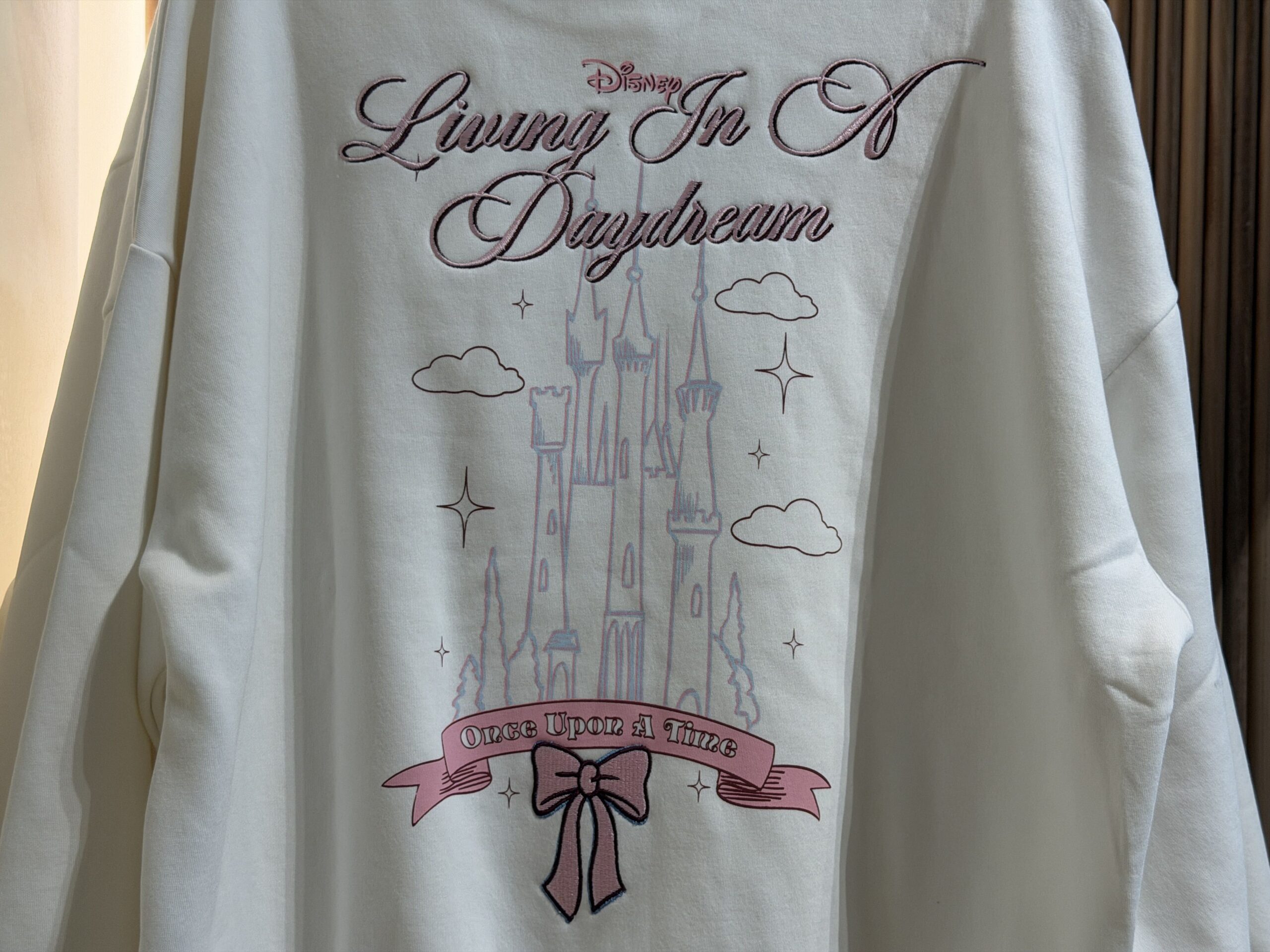 The back of the sweatshirt has a large castle surrounded by clouds and stars. "Living In A Daydream" is embroidered above the castle, while the same "Once Upon a Time" scroll design is below.