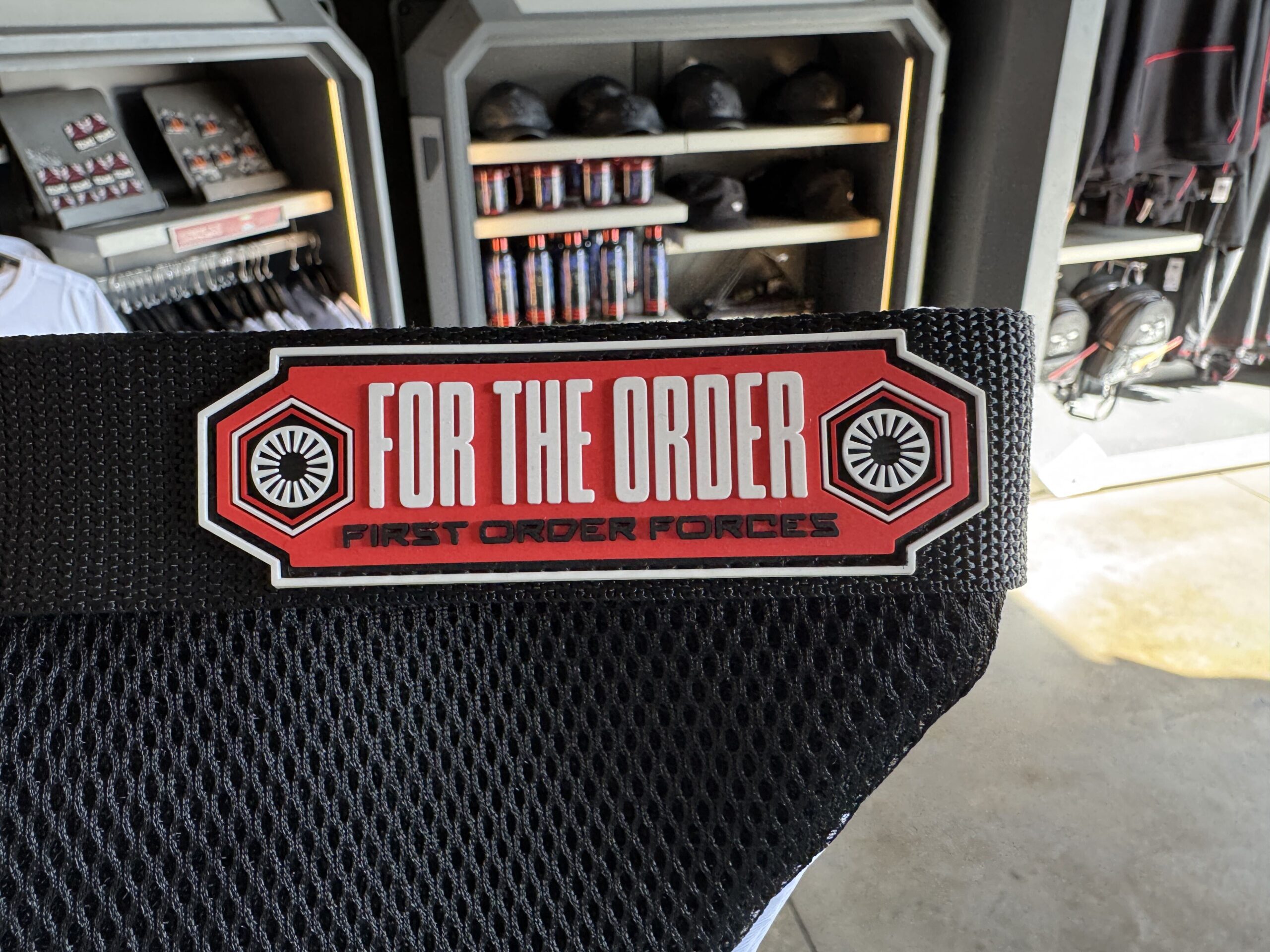 The back is black padded mesh. On the black adjustable strap for wear is a red label reading "FOR THE ORDER" largely in white. Below reads "FIRST ORDER FORCES" smaller, in black. The sides of the label feature the First Order symbol.
