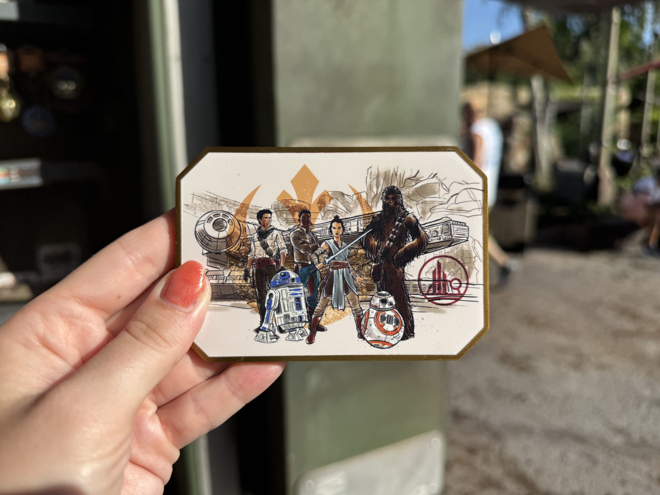 This magnet celebrates the Resistance, featuring Rey, Finn, Poe, Chewbacca, BB-8, and R2-D2 in front of a Resistance ship in a sketched animation style. Rey stands front and center, ready for battle with her blue lightsaber alight, and is flanked by her cohorts. Behind them, faded in the background, is a large orange Resistance emblem.