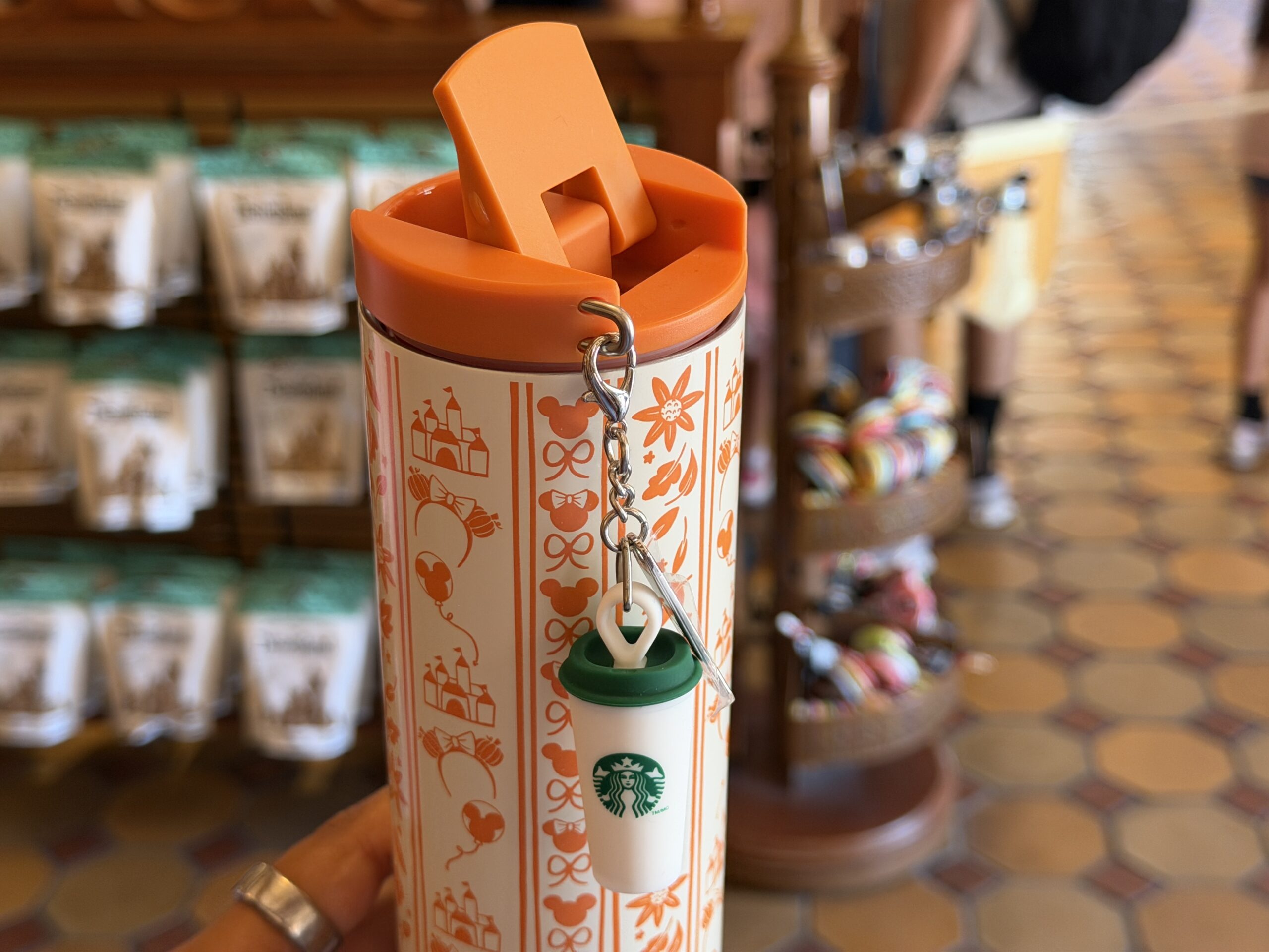 Included is a Starbucks cup-shaped silicone charm featuring a green lid and Minnie pumpkin. The lid is orange.