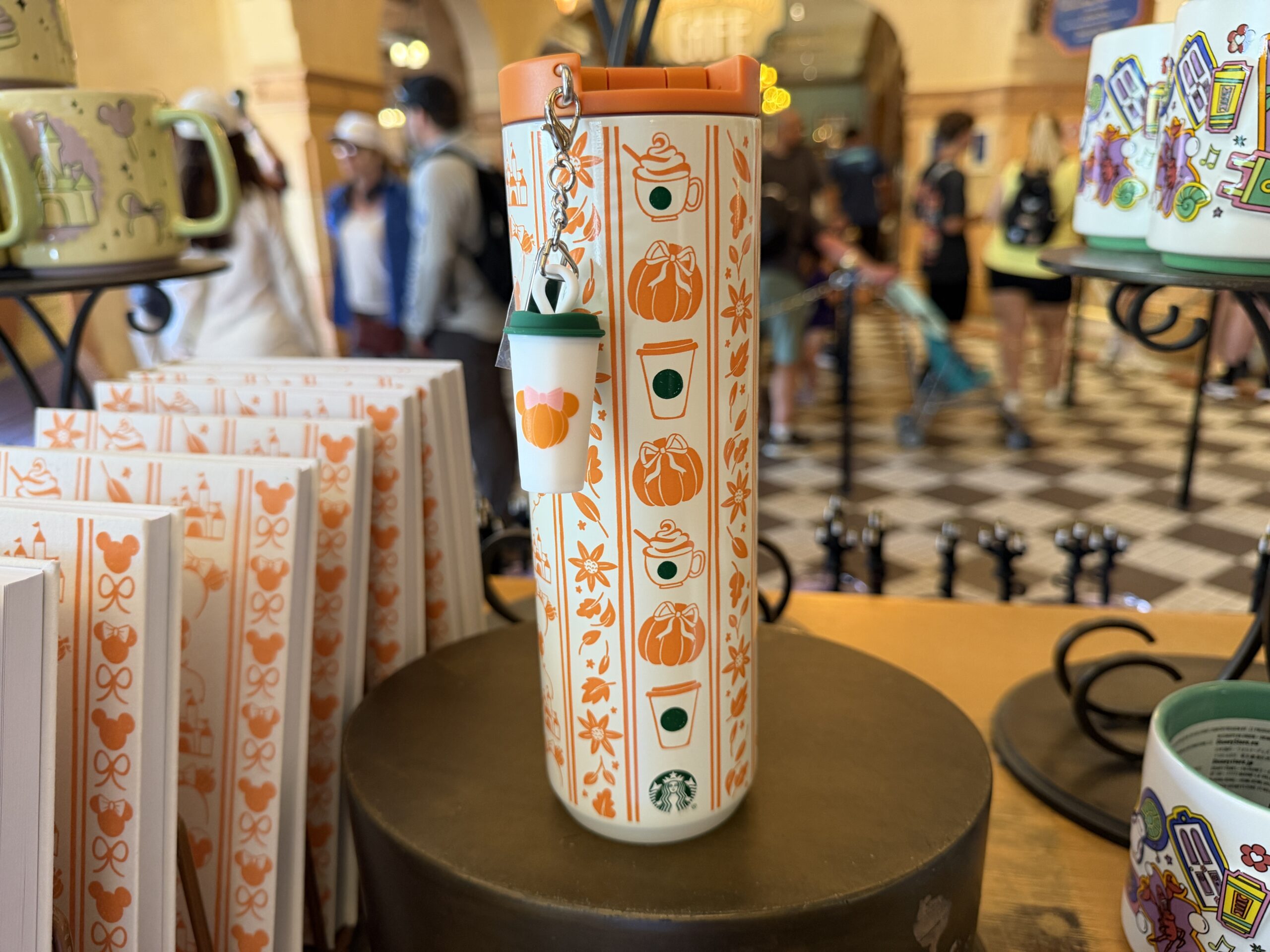 The stainless steel bottle is white with rows of orange designs autumnal leaves and flowers. One row features pumpkins topped with bows and Starbucks drinks with green accents.