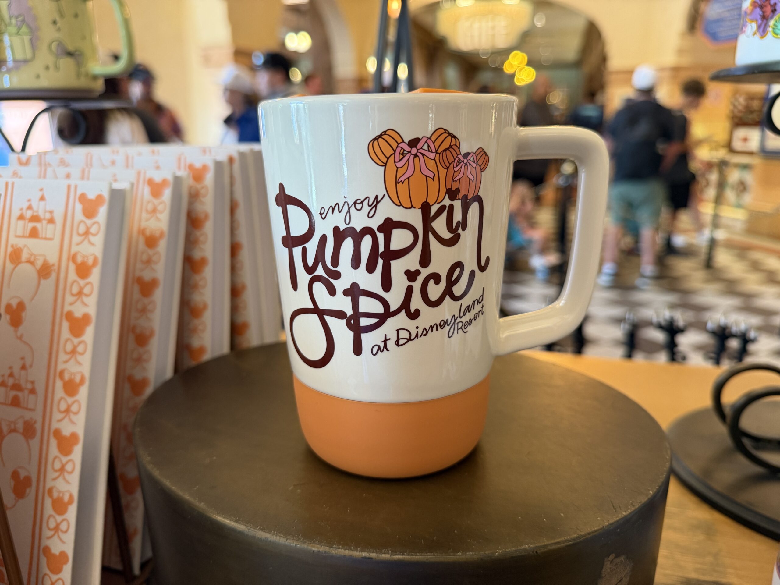 The stoneware mug is white with an orange base and lid. "Enjoy pumpkin spice at Disneyland Resort" is on one side with two Minnie pumpkins wearing bows.