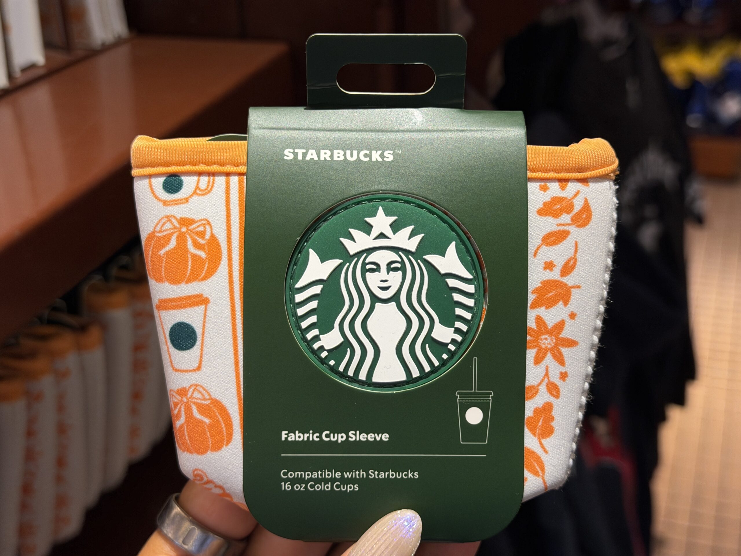 The cup sleeve features the same orange pattern as the bottle. The Starbucks logo is on one side. This size is compatible with Starbucks 16 oz cold cups.