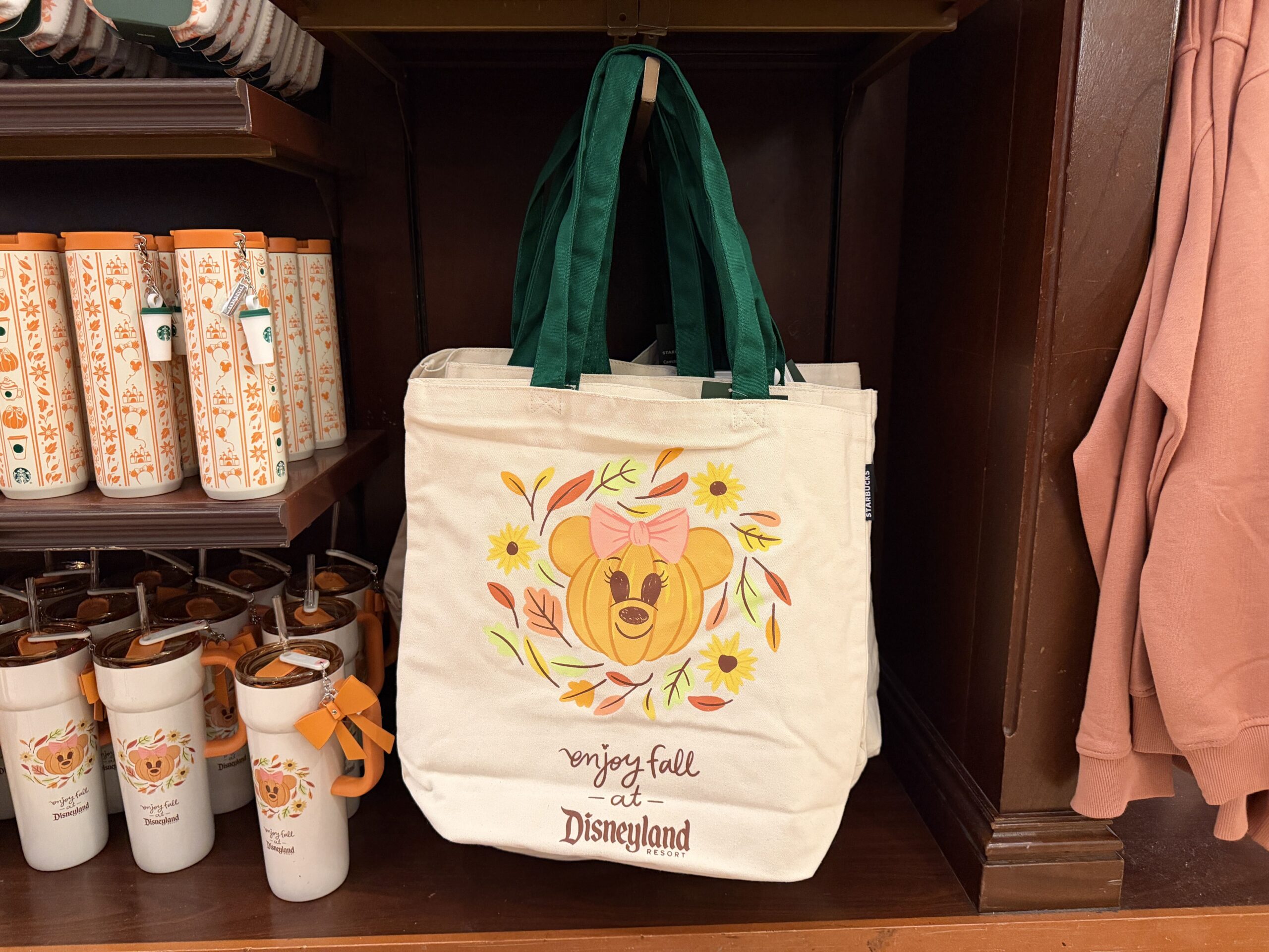 The canvas tote has the same Minnie pumpkin artwork from the tumbler with "Enjoy fall at Disneyland Resort." It has two green shoulder straps.