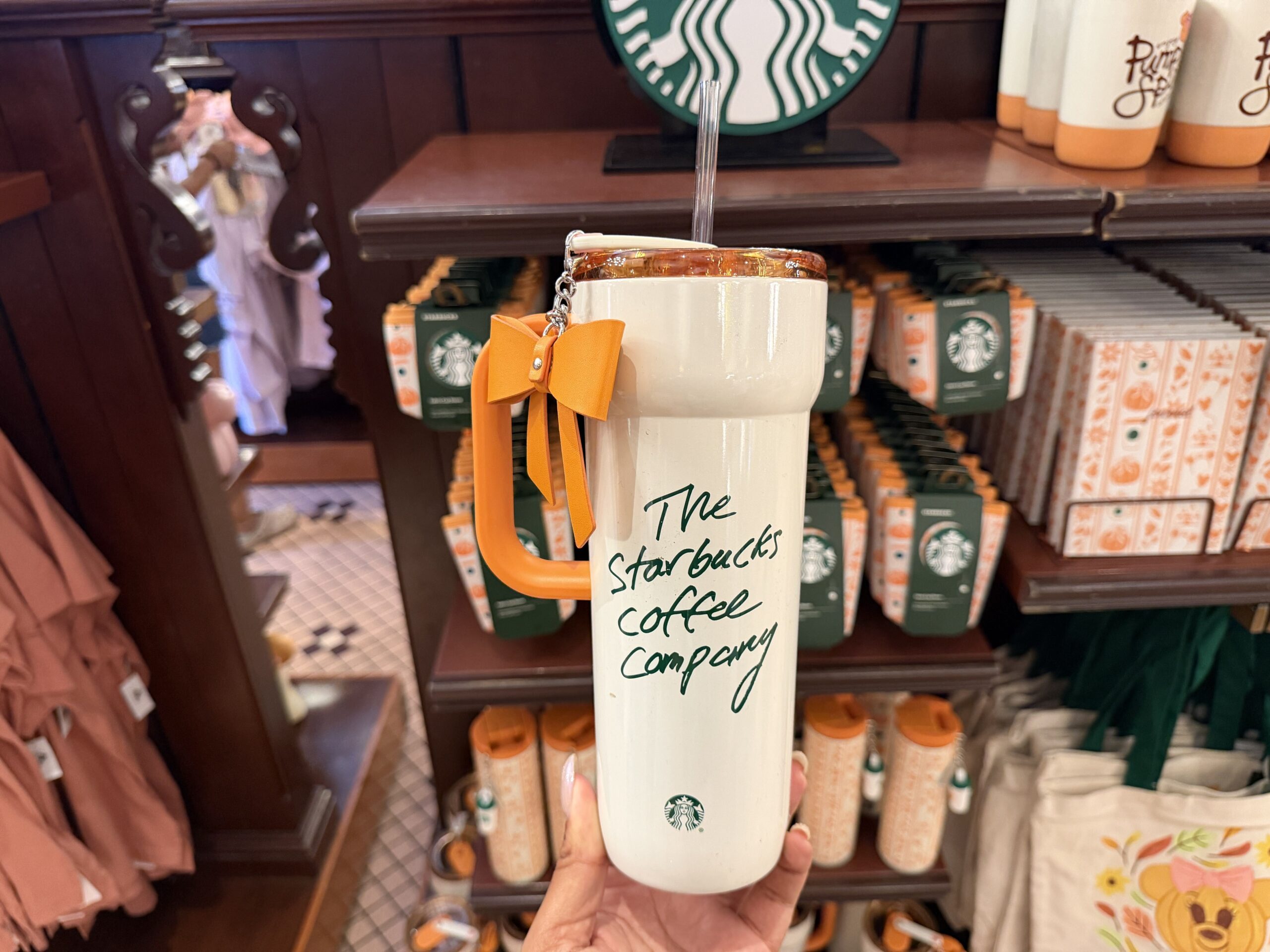 "The Starbucks Coffee Company" is in green on the other side. The included charm is an orange faux leather bow featuring a Mickey icon.