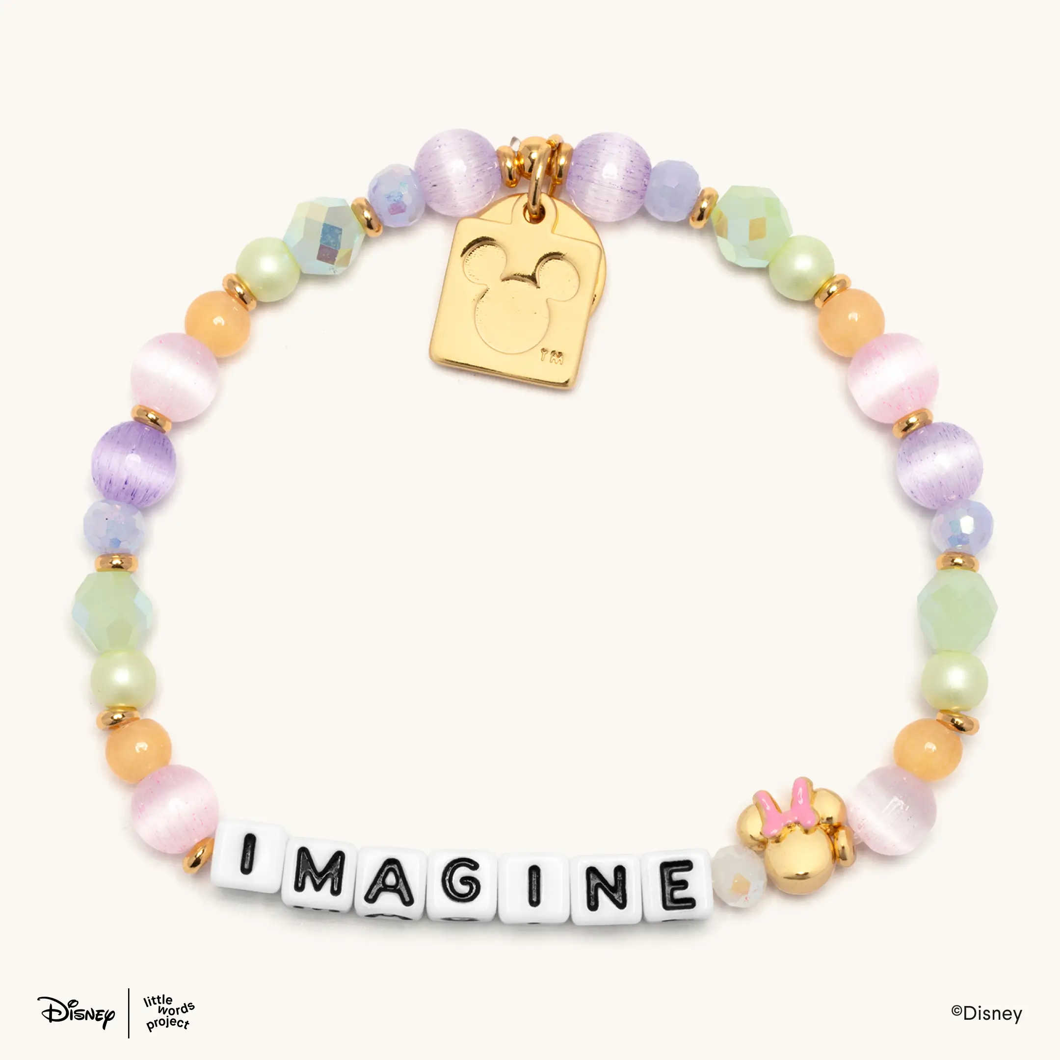 This rainbow-beaded bracelet spells "IMAGINE" with white letter blocks. A gold Minnie head charm with a pink bow is attached next to the word.