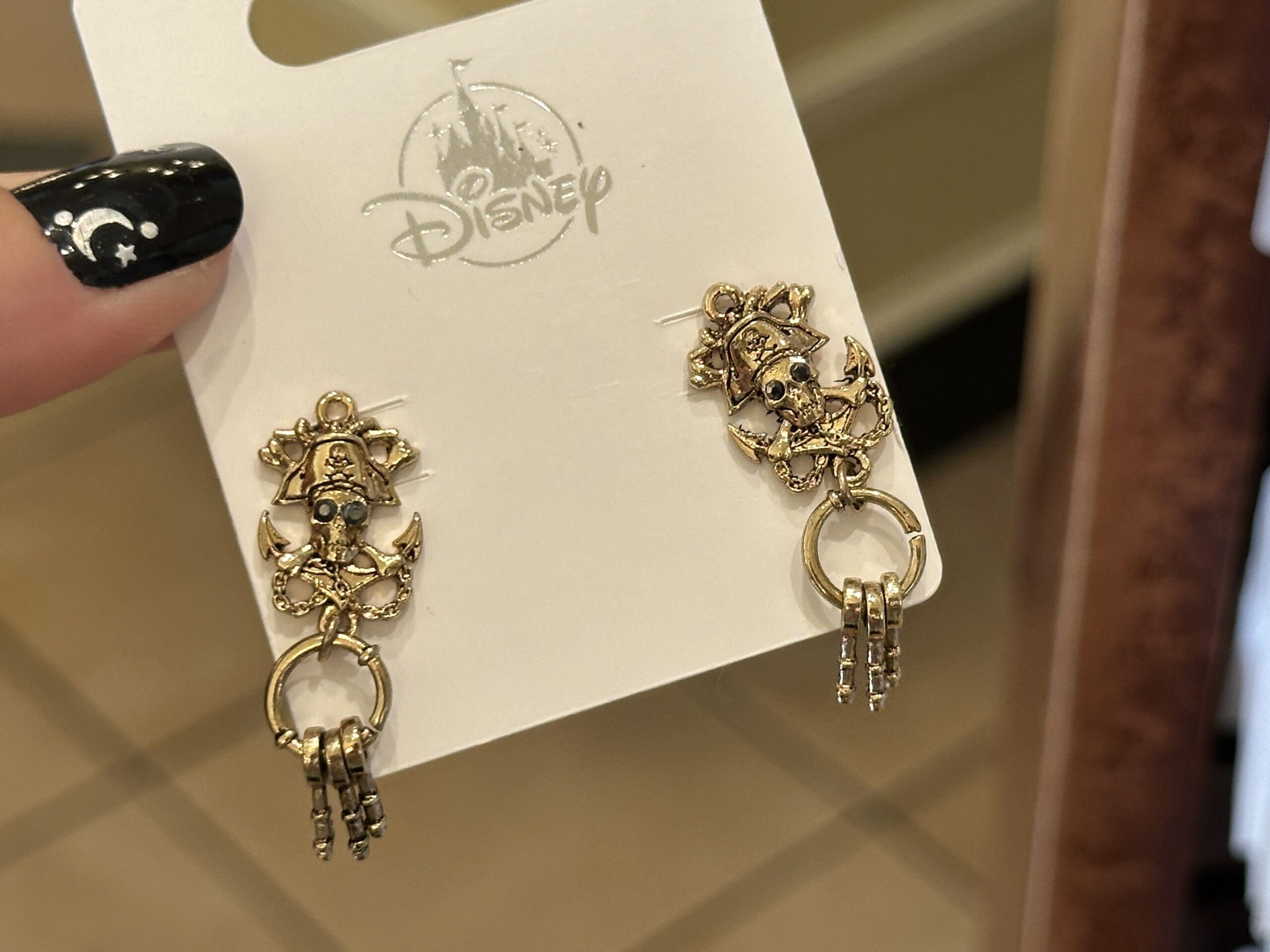 A set of earrings matches the necklace in the same gold tone, featuring skulls and crossbones with black jeweled eyes overlaying an anchor and chains, with a key ring featuring three keys on each earring.