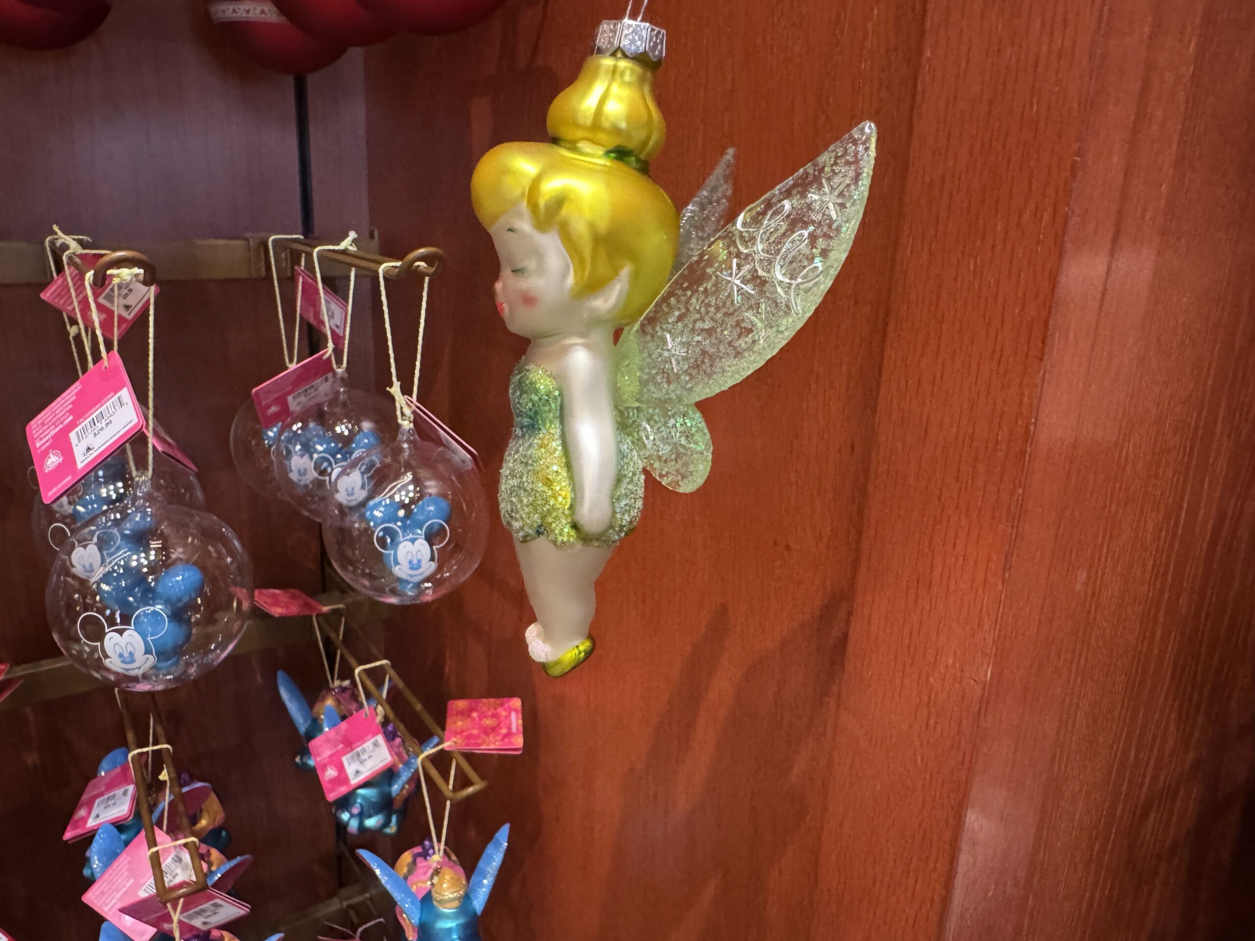 This Tinker Bell ornament is a cherub-like version of Peter Pan's partner in crime. She is crafted of porcelain and painted in a watercolor style with bright colors.  Her dress and the pom poms on her shoes glitter. She has rosy cheeks and is smiling with her eyes closed in joy. 