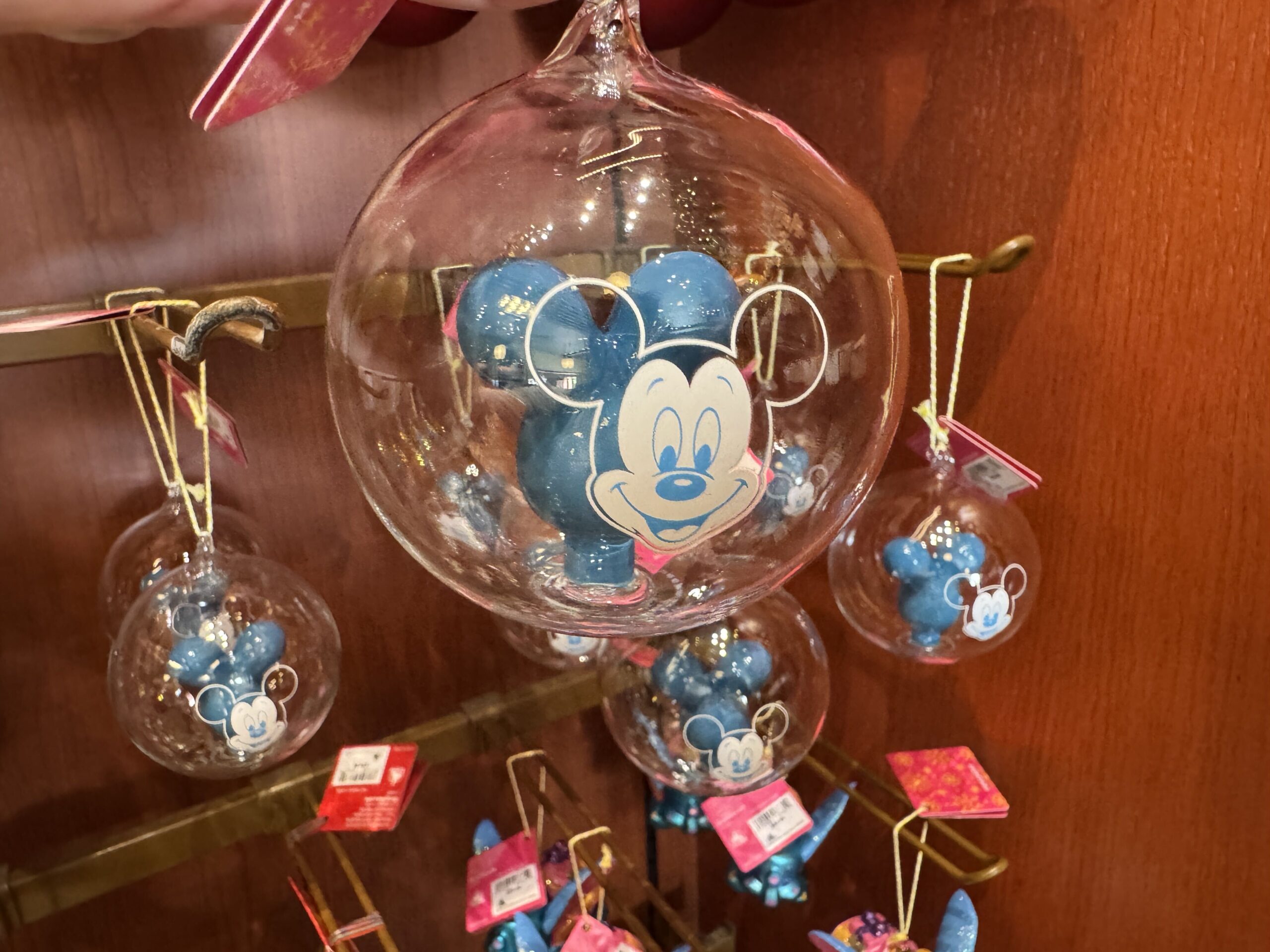 This clear glass ornament features a classic blue Mickey balloon inside. The front of the glass is painted with Mickey's face in white, mimicking a Main Street Mickey Balloon in miniature form.