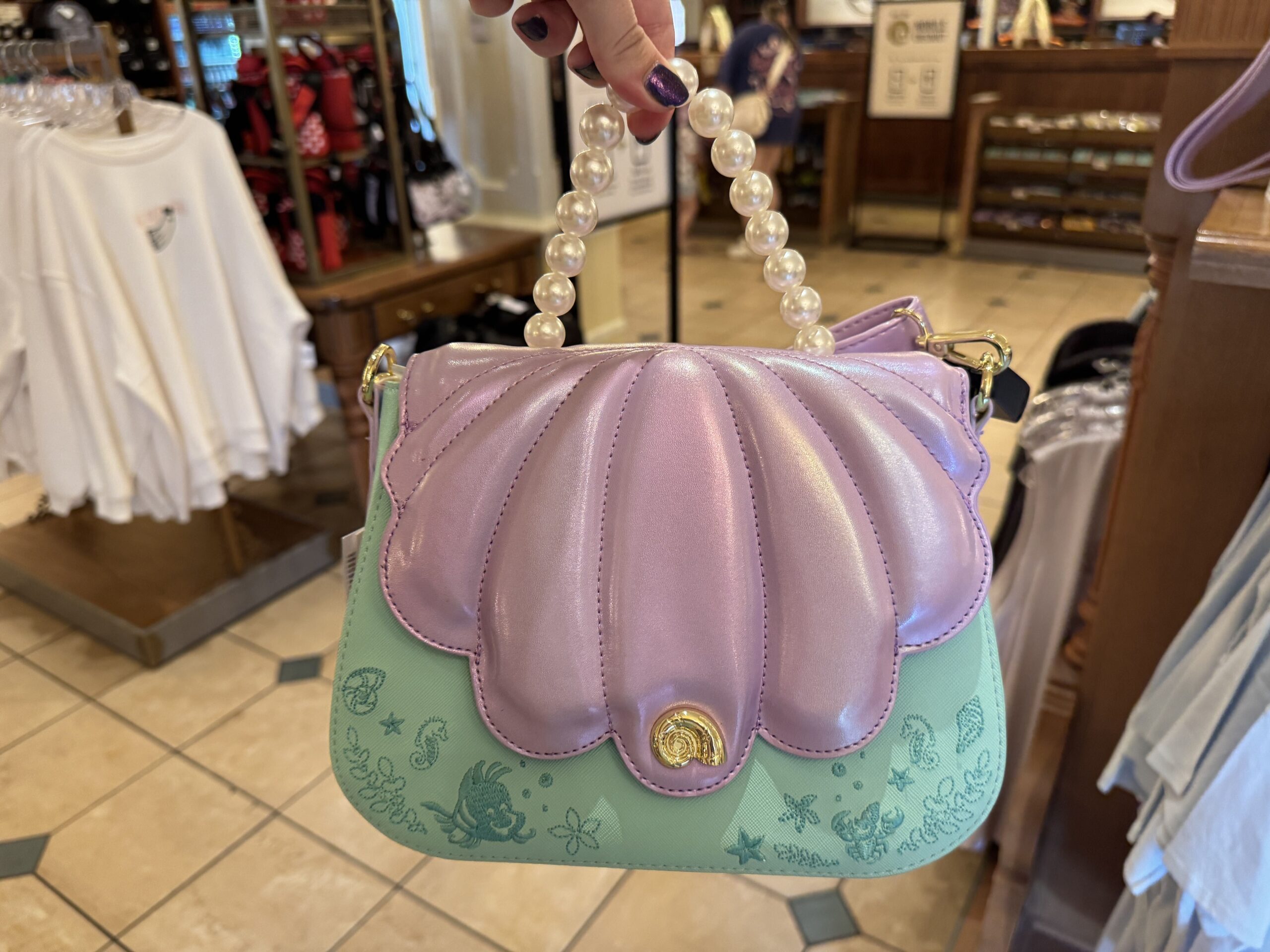 The Ariel-inspired Loungefly bag is constructed of a teal leather body embroidered with images of seashells, seahorses, starfish, seaweed, and her sidekicks, Flounder and Sebastian, around the edges. 

The flap of the purse is purple leather matching the style of Ariel's seashells, and is anchored with a gold-toned metal seashell. A handle from the top of the bag is strung with pearls.