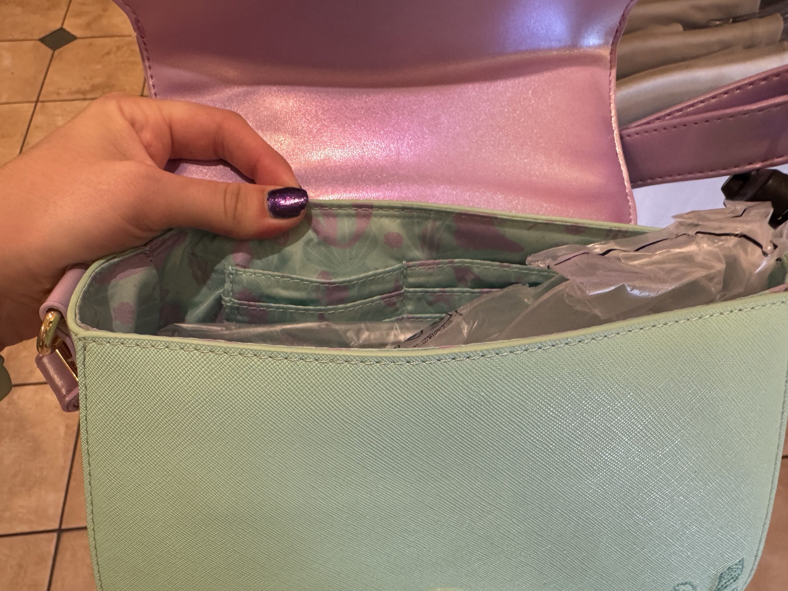 The inside of the handbag is lined with teal fabric featuring images of purple and teal seashells. There are six card slots inside.

The bag closes with a magnetic clasp and is wearable with an adjustable strap.
