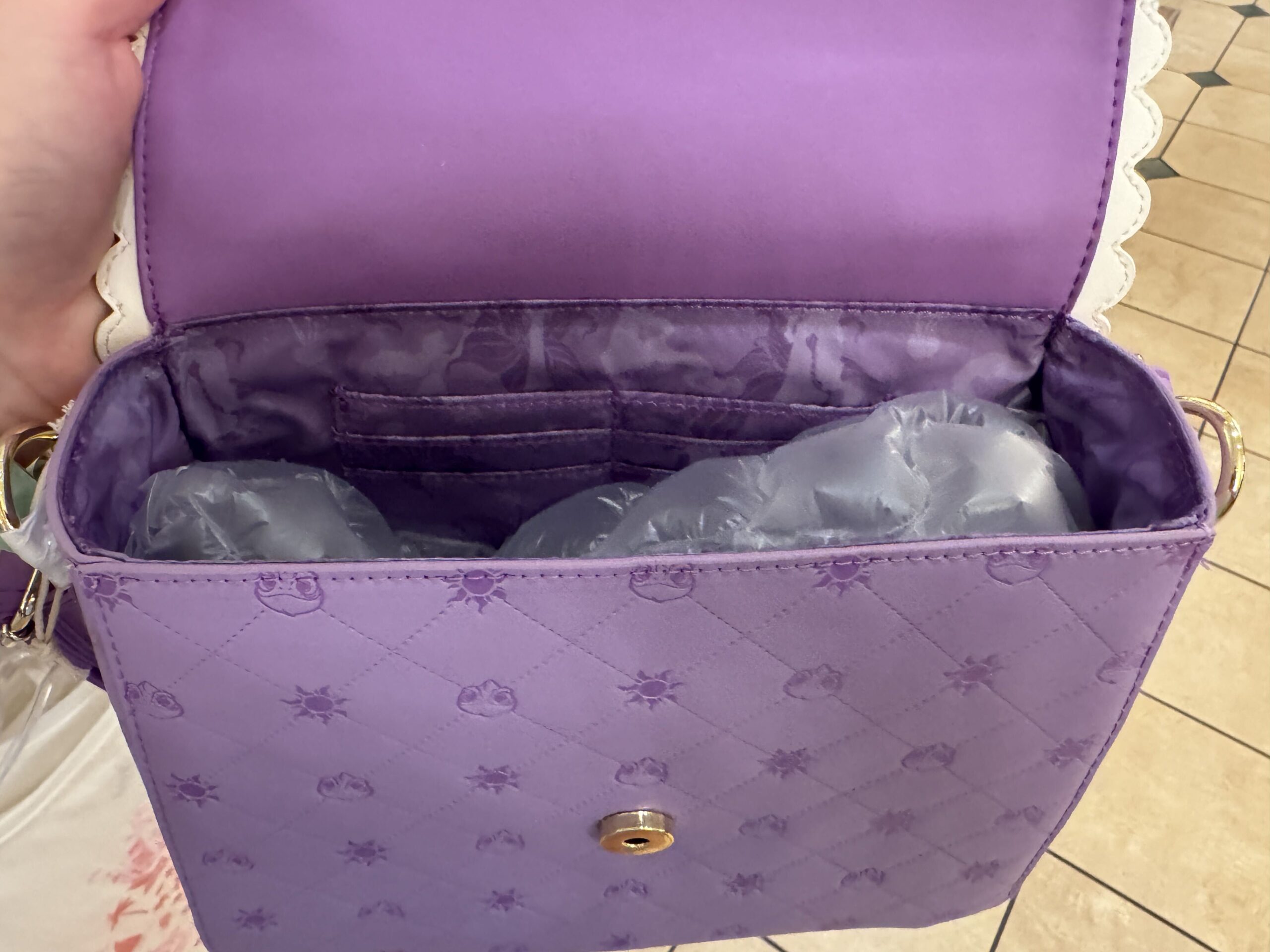 The inside of the handbag is lined with purple fabric featuring images of flowers and suns in various shades of purple. There are six card slots inside.

The bag closes with a magnetic clasp and is wearable with an adjustable strap.