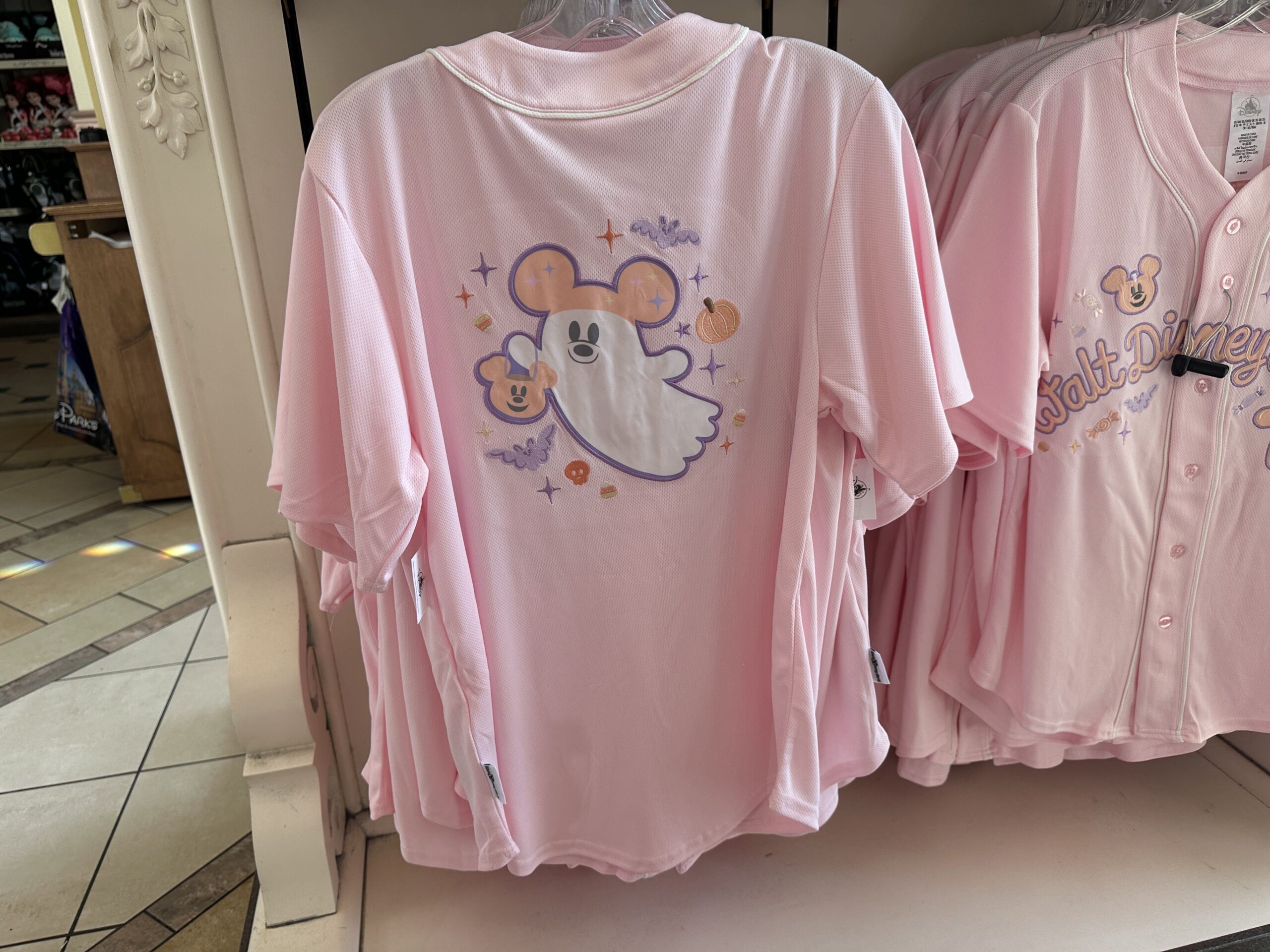 The sports jersey buttons down the front and features "hey boo" text surrounded by a Mickey pumpkin, bat, and sparkles. The back has a large image of a Mickey ghost holding a candy bucket. He is surrounded by jack-o'-lanterns, bats, and sparkles.