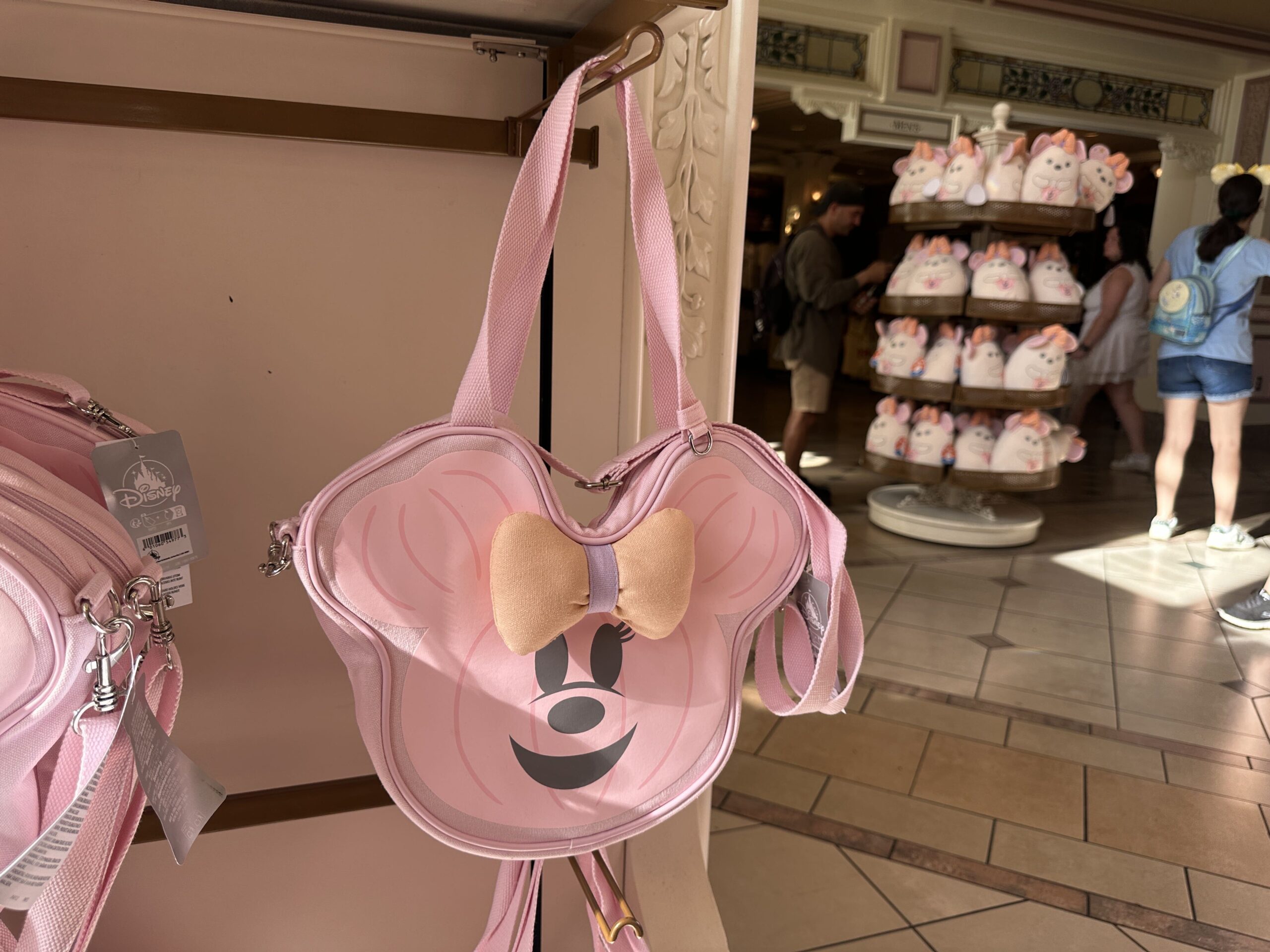 A pastel pink face tote is part of the collection. Shaped like a jack-o'-lantern, Minnie has a three-dimensional orange and purple bow. The back say "hey boo" and has a Mickey ghost. It has a shoulder strap, as well as a secondary strap that can be removed.