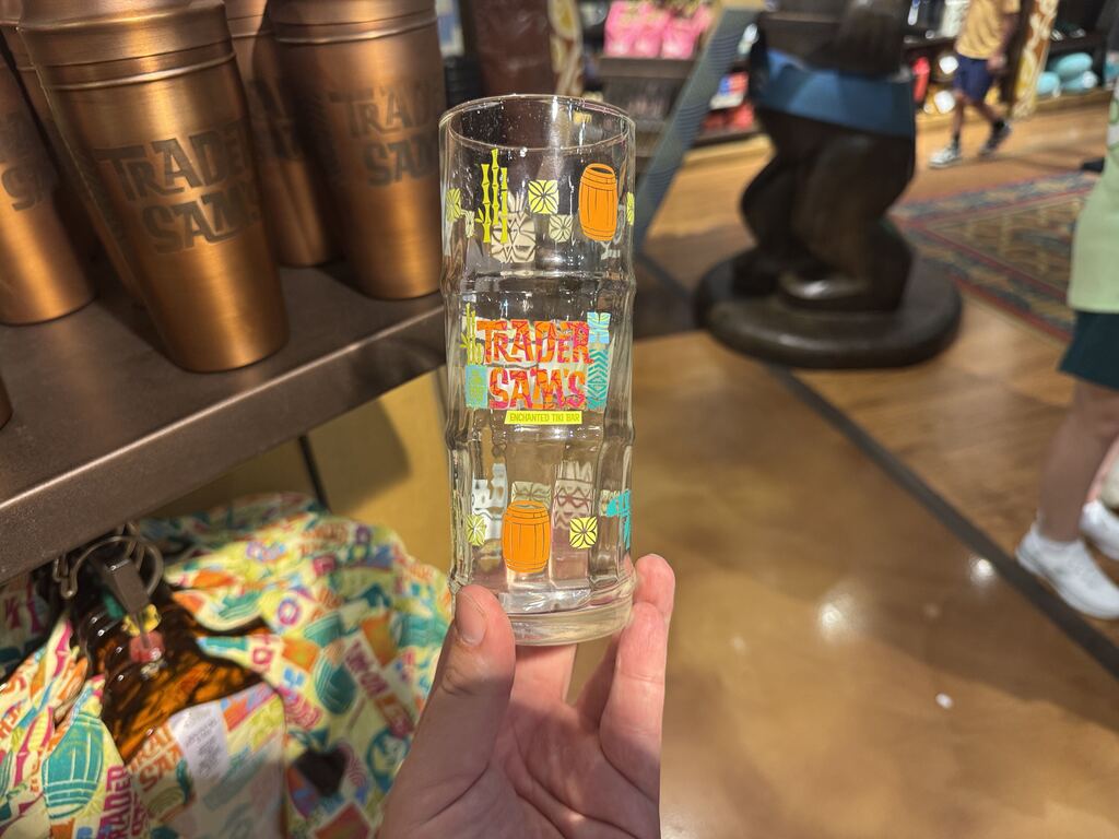It has a colorful exterior with a mix of pink, yellow, teal, and orange. The front reads "Trader Sam's" in orange and pink with "Enchanted Tiki Bar" written in yellow underneath.